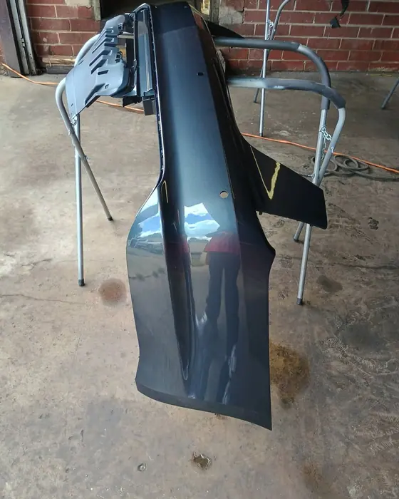 A rear bumper cover refinished in gloss black, up on stands in the shop