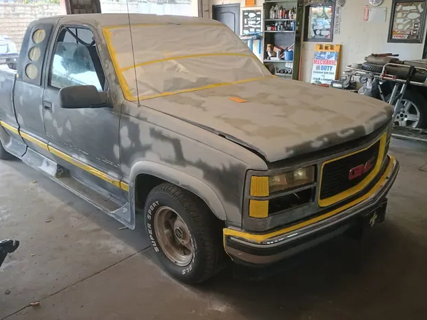 A GMC pickup in primer with its glass and trim masked off in the bay