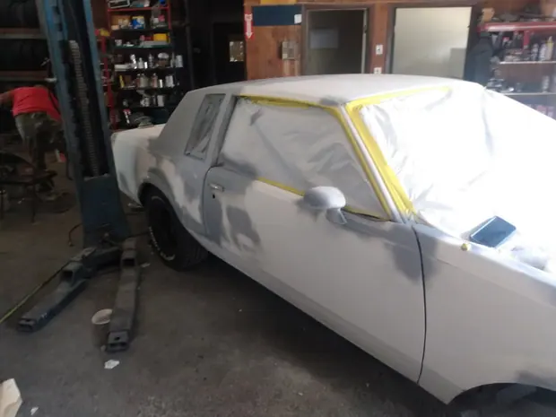 An older coupe in primer with its glass masked, partway through the bodywork